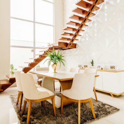 Minimalistic design of spacious room with second level space and wooden staircase against large windows in modern house in daytime